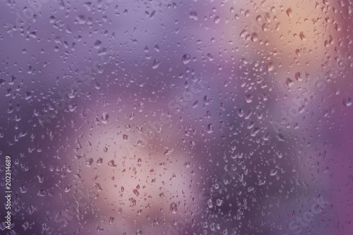 Abstract violet and orange background, texture of rain drops on glass. Raindrops on window, rainy weather.