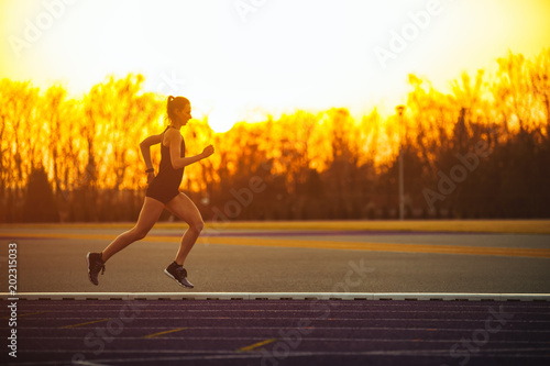Athletic woman running on racetrack during sunset