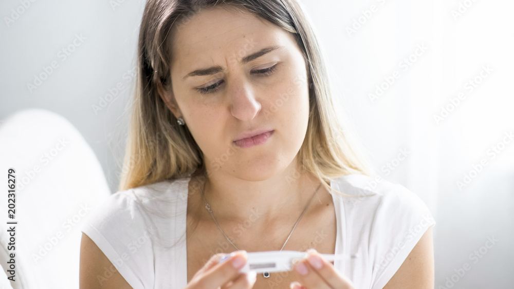 Closeup portrait of young woman with cold sitting on sofa with thermometer