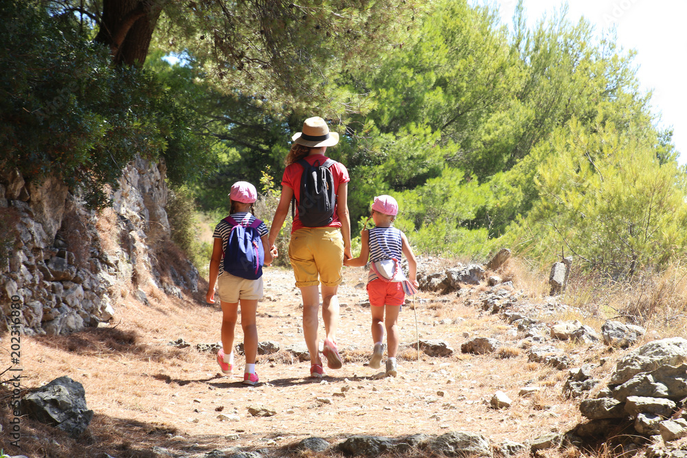 Mom with two daughters travels along a beautiful path in the mountains over the sea.