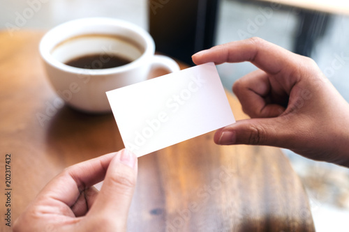 Hands holding an empty business card with coffee cup on table