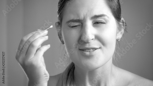 Black and white portrait of young woman feeling pain after plucking eyebrows at mirror photo