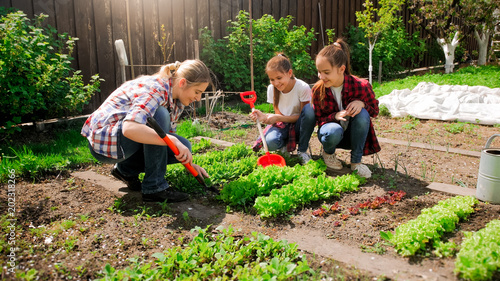 Happy young woman with daughters planting seeds in garden