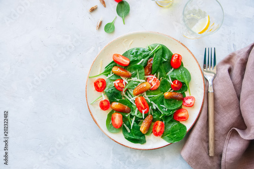 Fresh salad with spinach tomatoes cherry and dates served on a plate. White stone background. Healthy eating concept.