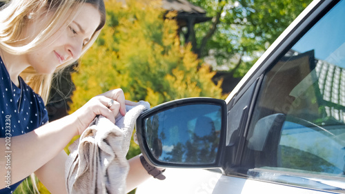 Portrait of beautiful smiling woman cleaning car mirrors at backyard