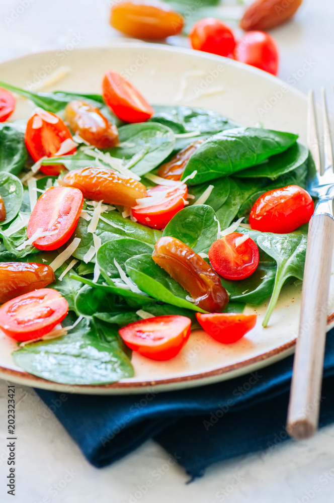 Fresh salad with spinach tomatoes cherry and dates served on a plate. White stone background. Healthy eating concept. Fresh salad with spinach tomatoes cherry and dates served on a plate. White stone background. Healthy eating concept.