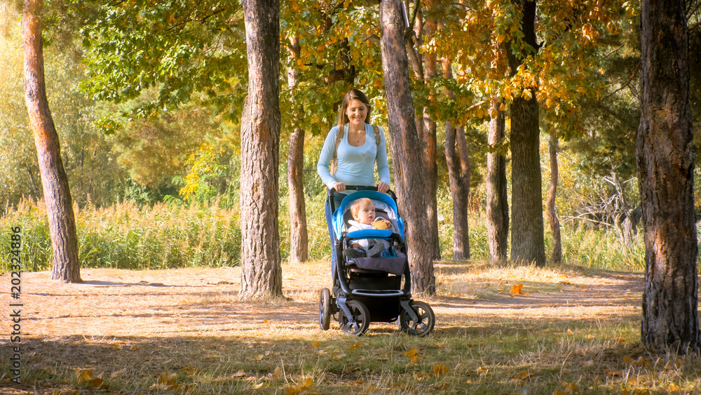 Beautiful smiling mother walking in park with her toddler son sitting in pram