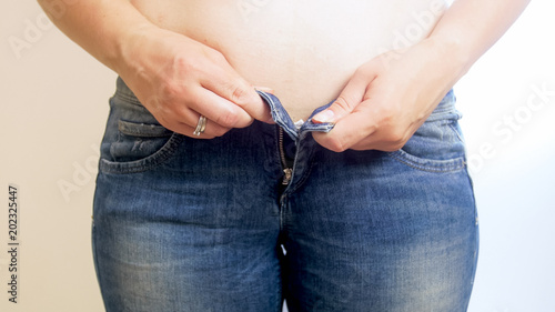 Closeup image of young overweight woman trying to put on tught jeans photo