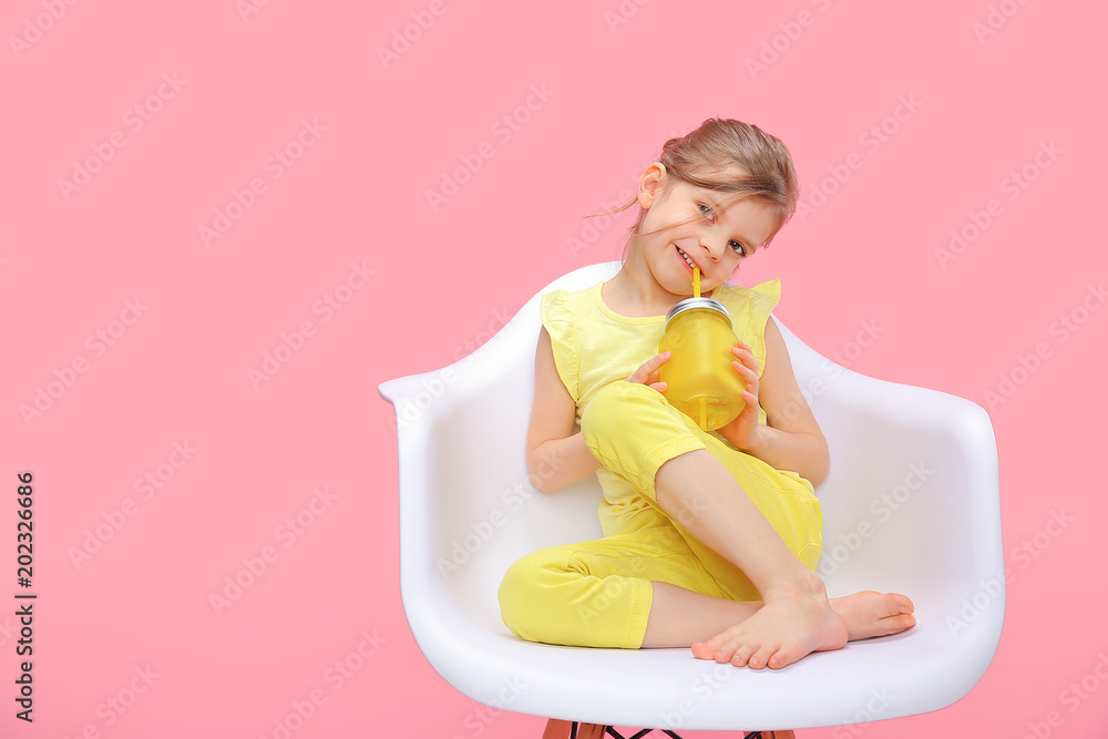 Φωτογραφία Charming little girl in yellow sitting in chair and smiling holding glass with lemonade and straw on pink background
