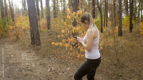 Portrait of young sporty woman choosing music on smartphone while jogging in forest © Кирилл Рыжов