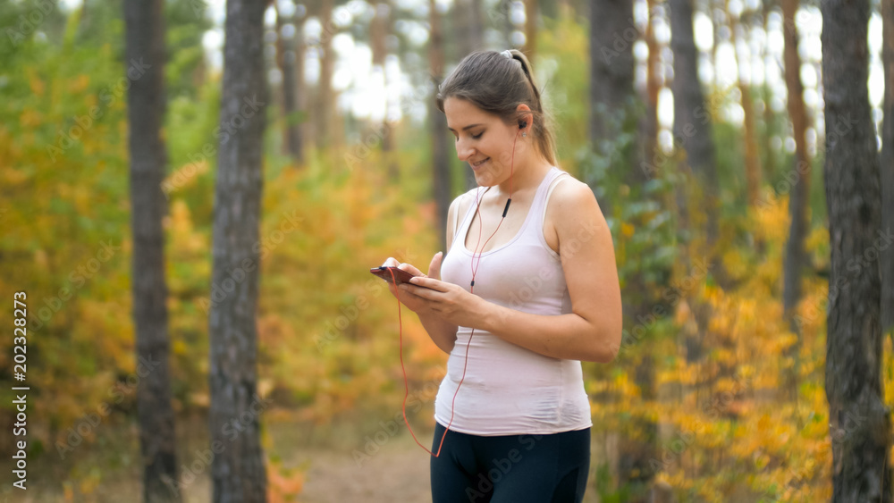 Toned portrait of young smiling woman choosing music before jogging in forest Toned portrait of young smiling woman choosing music before jogging in forest