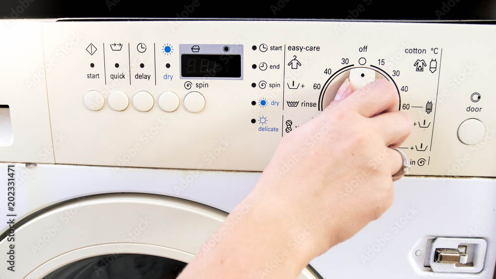 Closeup photo of female hand adjusting and setting washing machine at laundry Closeup photo of female hand adjusting and setting washing machine at laundry