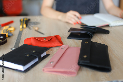 Handmade leather woman wallets and notebook on table at atelier near tools. Concept of home business, handicraft and hobby. photo