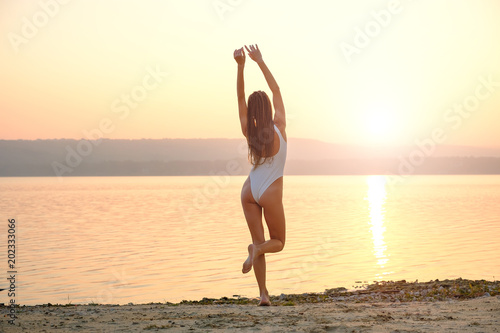 Young woman in strings swimsuit stands on the beach in sunrise  © arthurhidden