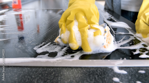 Closeup image of hand in yellow rubber glove holding sponge with suds photo