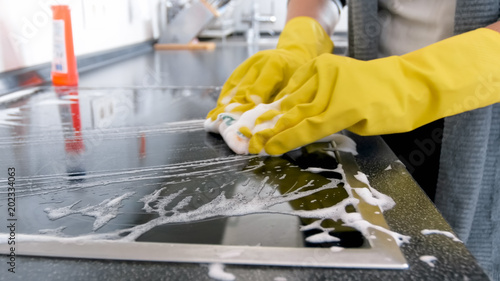 Closeup image of young woman in gloves washing electric cooker surface photo