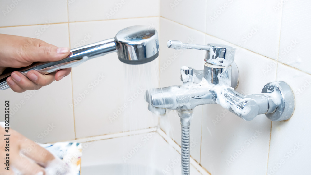 Closeup image of young woman cleaning water faucet in bathroom Closeup image of young woman cleaning water faucet in bathroom
