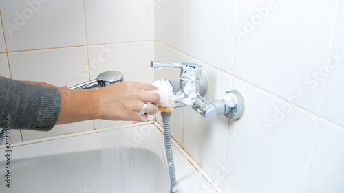 Closeup image of young woman cleaning water faucet in bathroom with detergent