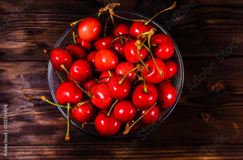 Fresh ripe cherries in glass bowl on wooden table. Top view