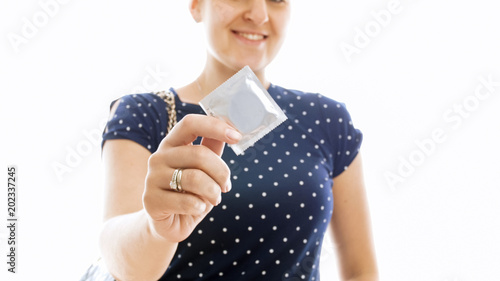 Closeup photo of young smiling woman showing condom in camera