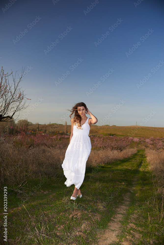 Pretty blonde in a white dress walking among the peach trees Pretty blonde in a white dress walking among the peach trees