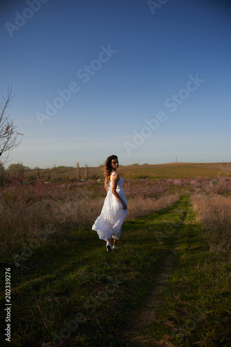 Pretty blonde in a white dress walking among the peach trees