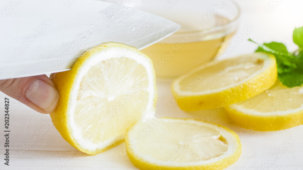 Closeup photo of sharp knife cutting fresh lemon in slices Closeup photo of sharp knife cutting fresh lemon in slices