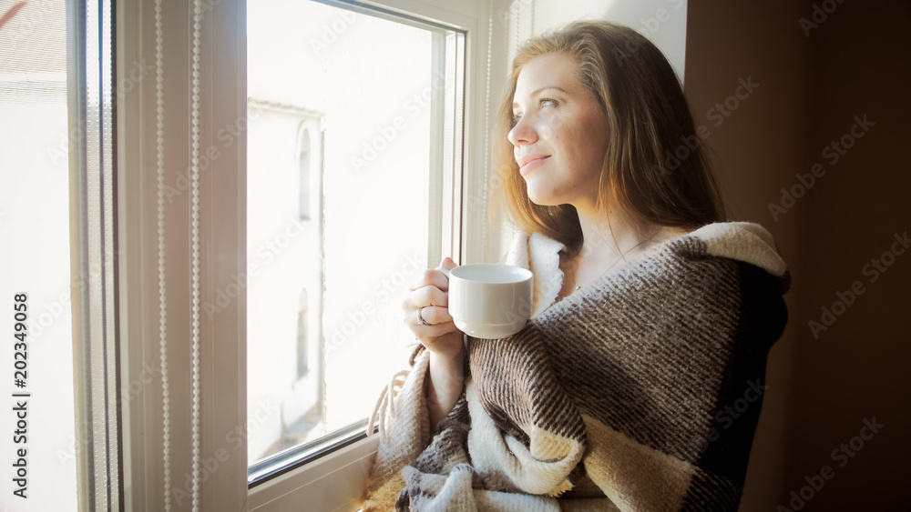 Αυτοκόλλητο Toned portrait of smiling young woman in plaid looking out of window