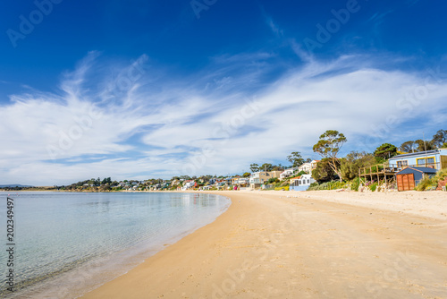 Pretty little to village town view with great paradise sandy beach with turquoise blue water and green covered rocks stone on warm sunny clear day for relaxing Opossum Bay, Hobart, Tasmania, Australia