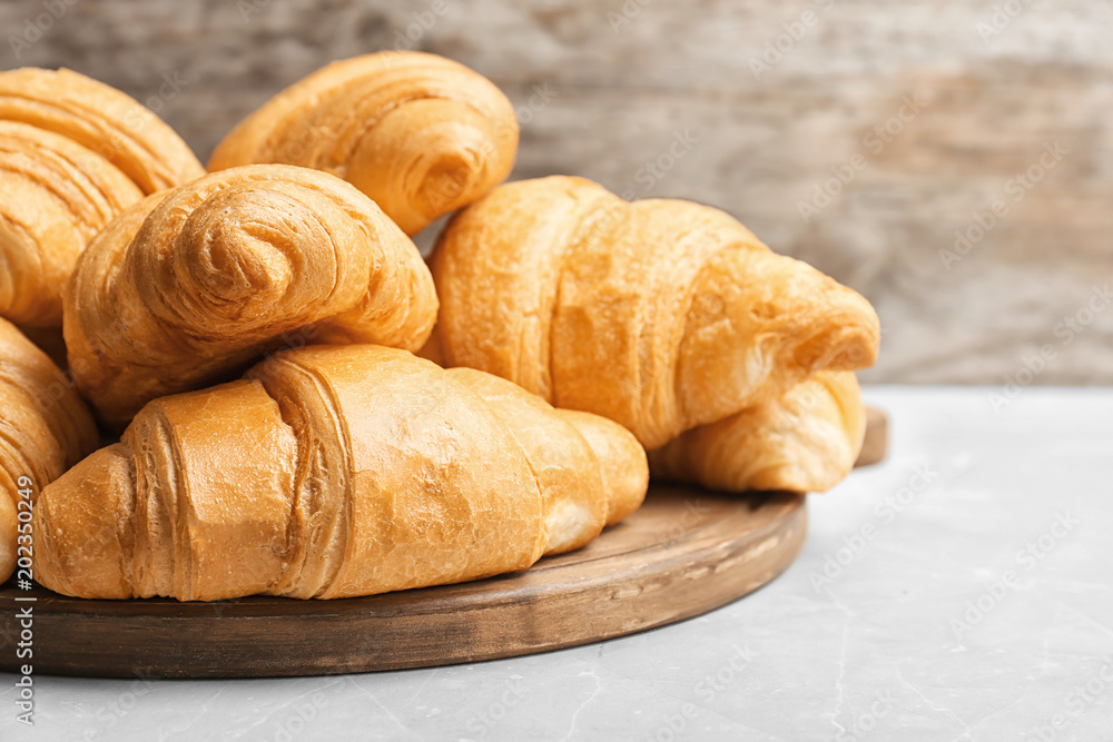 Wooden board with tasty croissants on table