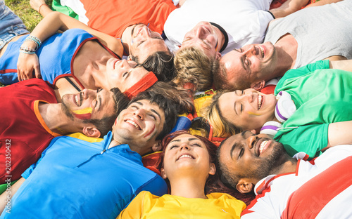 Happy friend group lying on meadow after world soccer event - Friendship concept with young people having fun at international sport festival - Football cup championship concept on warm bright filter