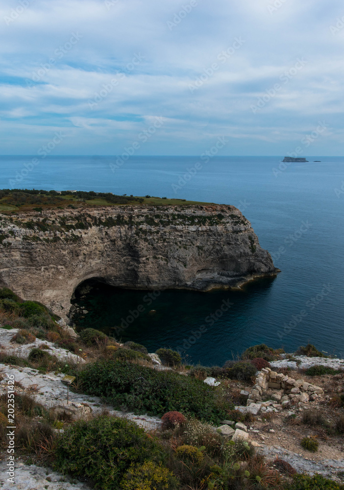 A cave at the bottom of the cliffs on a spring day with dramatic and cloudy sky and calm sea