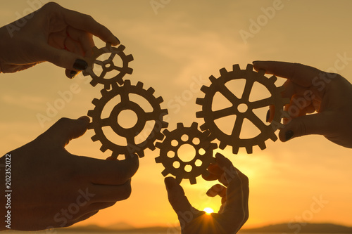 gears in the hands of people against the background of sunset. teamwork.