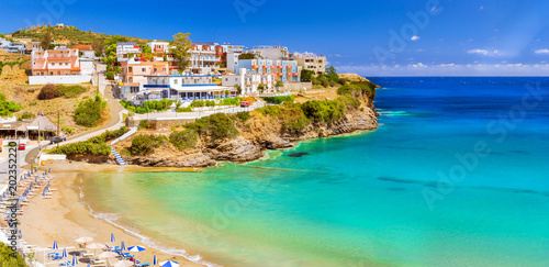 Sandy Varkotopos beach in sea bay of resort village Bali. Views of shore, washed by waves with sun loungers and parasols where sunbathing tourists. Greek houses stand on the rocky shore. Crete, Greece photo