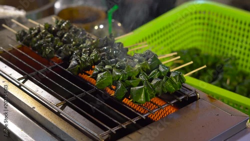 Process of making a barbecue of a minced meat wrapped in a palm leaves on a night market in Thailand. Thai food concept. Asian food concept photo