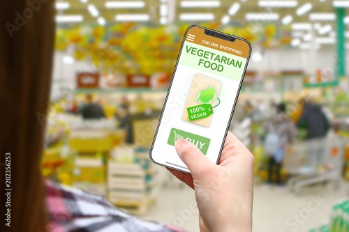Vegetarian food idea, girl with frameless phone on blurred shop background