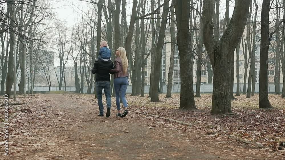 Happy family of three walks in the spring Park. Funny little boy sitting on his father's shoulders. Steadicam shot Happy family of three walks in the spring Park. Funny little boy sitting on his father's shoulders. Steadicam shot