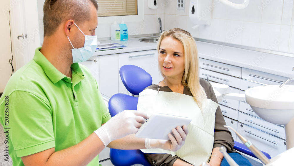 Beautiful young woman sitting in dentist chair and talking about treatment with doctor Beautiful young woman sitting in dentist chair and talking about treatment with doctor