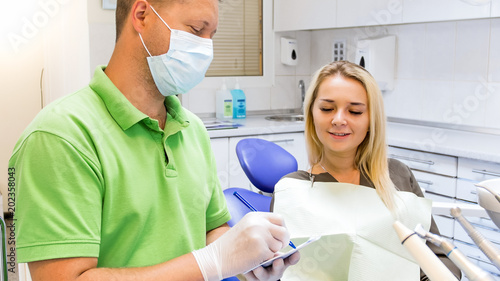 Beautiful young woman sitting in dentist chair and looking as doctor writes prescription
