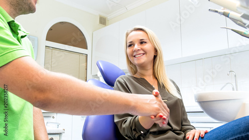 Happy smiling blonde woman shaking hands with male dentist in dental clinic