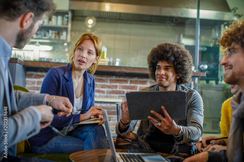 Afro american man talking with colleagues or clients using tablet.Group of multiethnic people having business team meeting in restaurant lounge.Teamwork,corporate,diversity and social concepts.