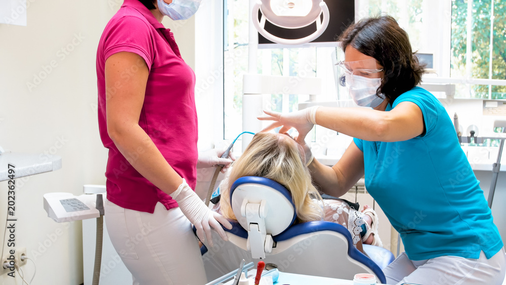 Female dentist with assistant preparing patient fo rteeth tretment Female dentist with assistant preparing patient fo rteeth tretment