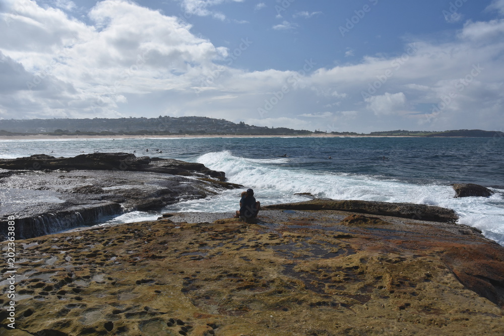 Young loving couple sitting on the rocks at Dee Why beach and watching the sea waves.