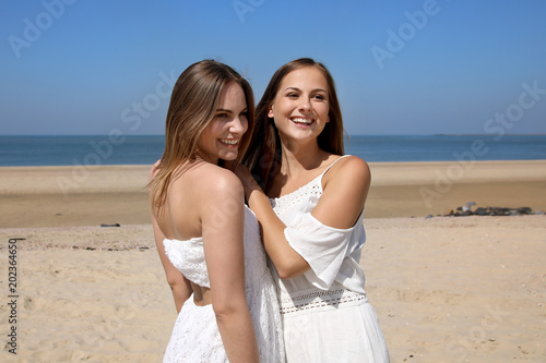 Zwei hübsche blonde Frauen umarmen sich am Strand und lachen