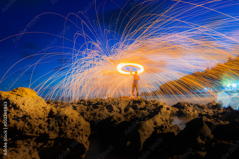 Φωτογραφία A ring of fire spinning steel wool on the rock and beach, Showers of hot glowing sparks from spinning steel wool on the rock and beach