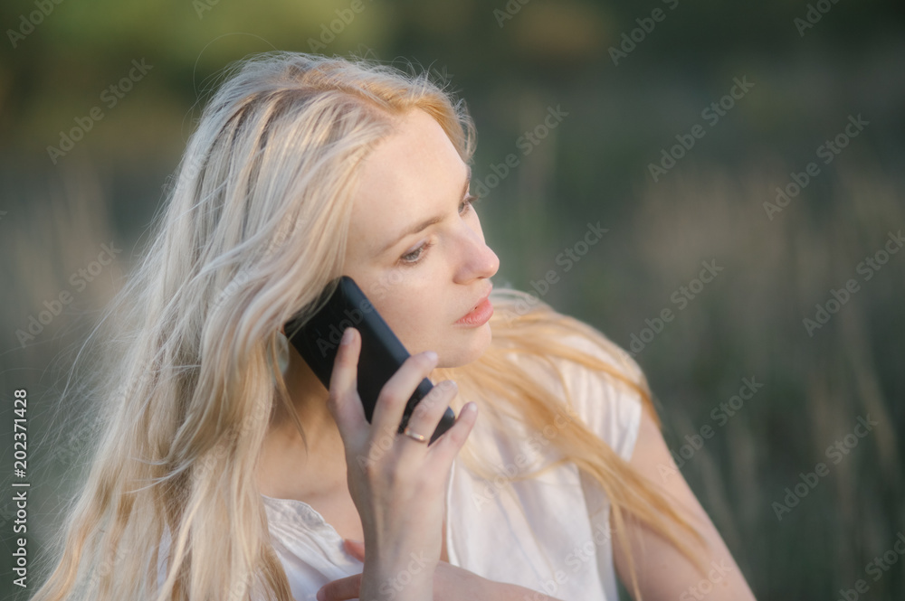 holding dress, boho beautiful blond woman in white dress in national park talking on the phone