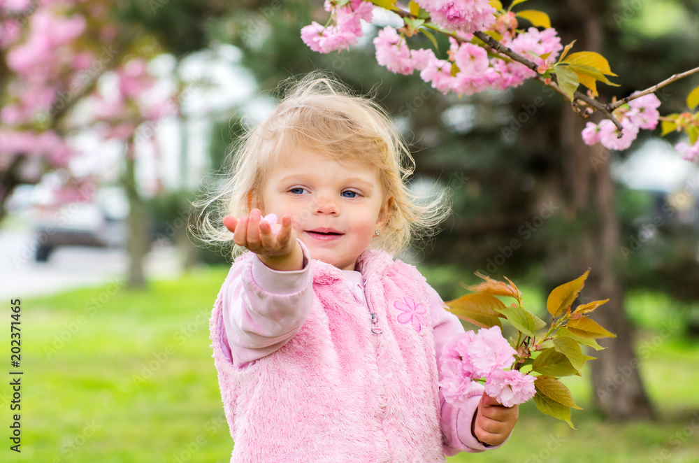 little charming blonde playing with pleasure in the garden with blooming cherry blossom little charming blonde playing with pleasure in the garden with blooming cherry blossom