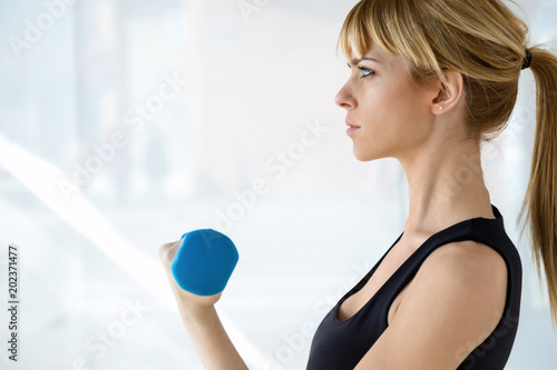 Sporty young woman doing muscular exercise with blue dumbbells in physio room.