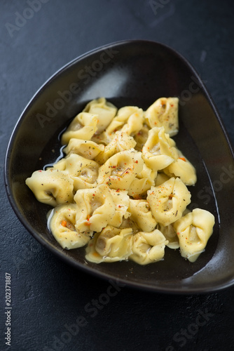 Closeup of a black bowl with tortellini served in bouillon, vertical shot, selective focus
