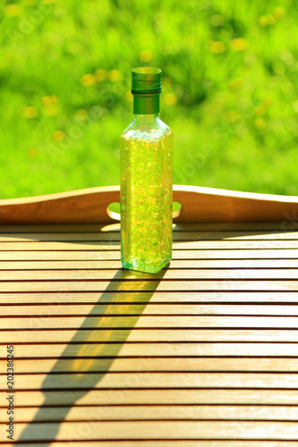 Kwadratowa butelka z olejem rzepakowym z czosnkiem i bazylją na drewnianej tacy.